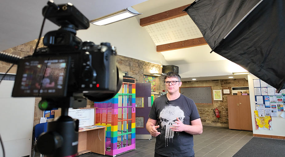 Behind-the-scenes of corporate interview setup in Teesside: man speaking to camera with cameraman and equipment visible – video production by Tees Vision Media