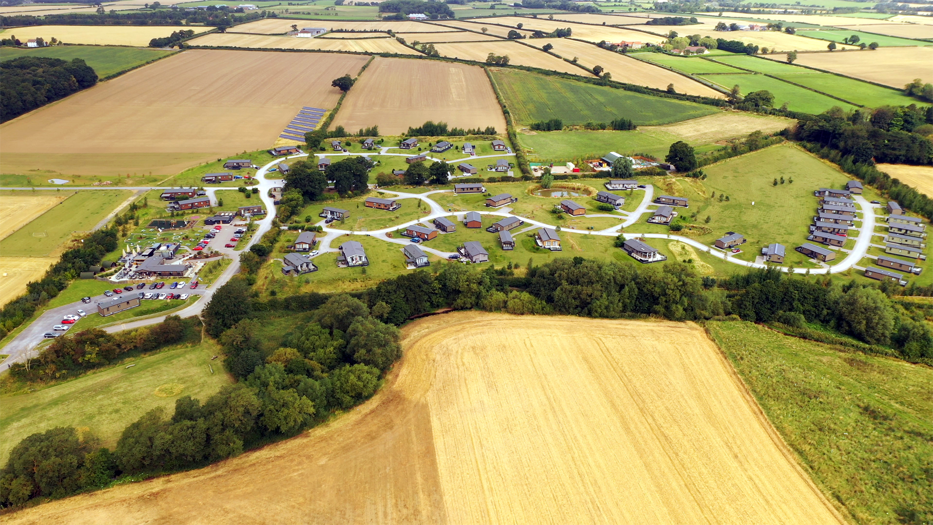 A high-altitude commercial drone photograph capturing a full bird's-eye overhead view of the entire Angrove Country Park lodge layout and surrounding Great Ayton countryside.