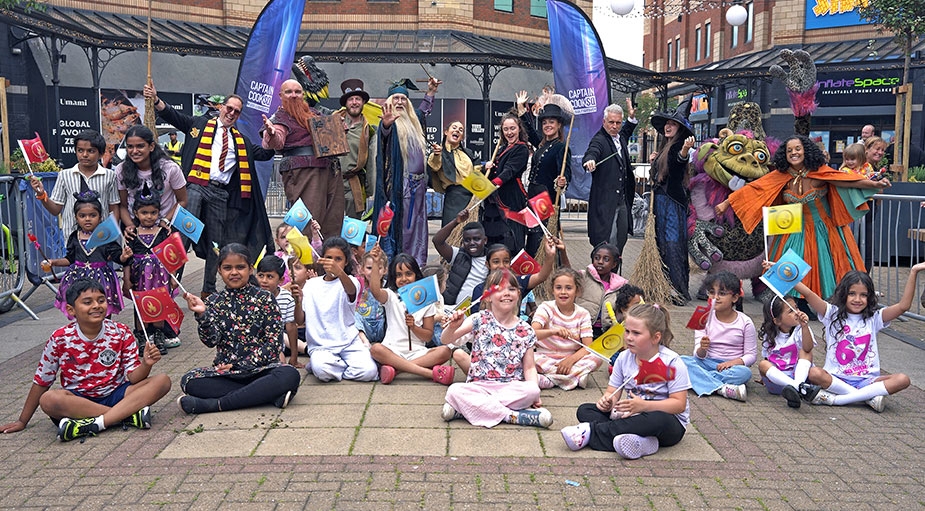 A wide-angle commercial group photograph of the entire performer cast and local children celebrating together at the end of a live public show in Captain Cook Square.