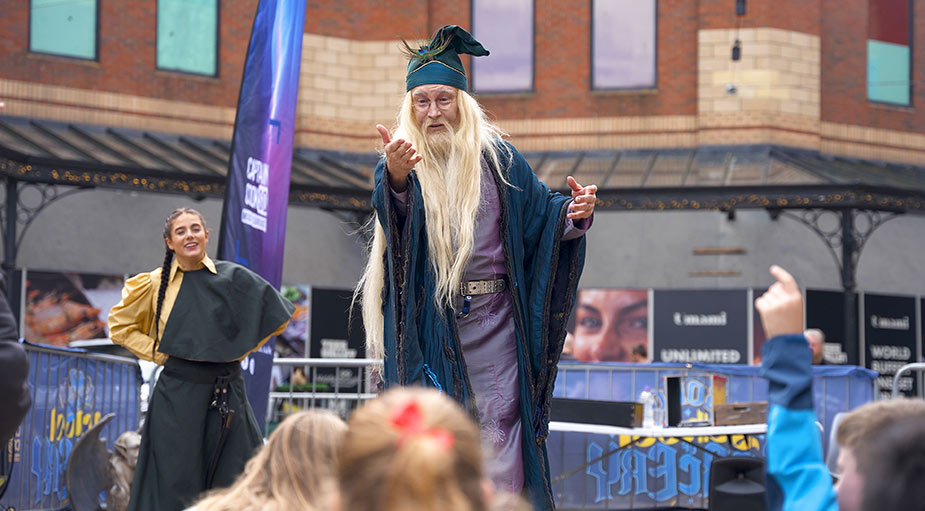 A candid event photograph of a wizard performer bringing a child volunteer up onto the stage during a live public crowd show in Middlesbrough.